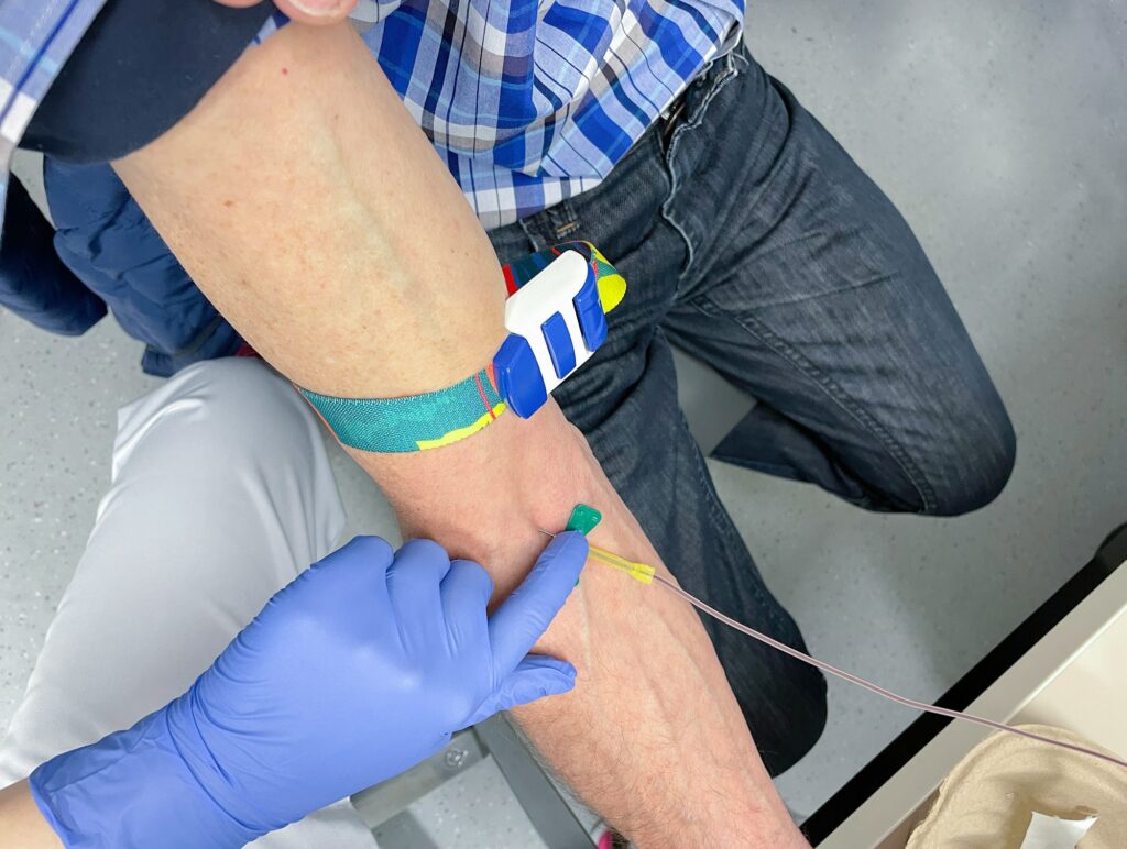 a nurse, doctor or medical technologist in blue gloves taking a blood sample